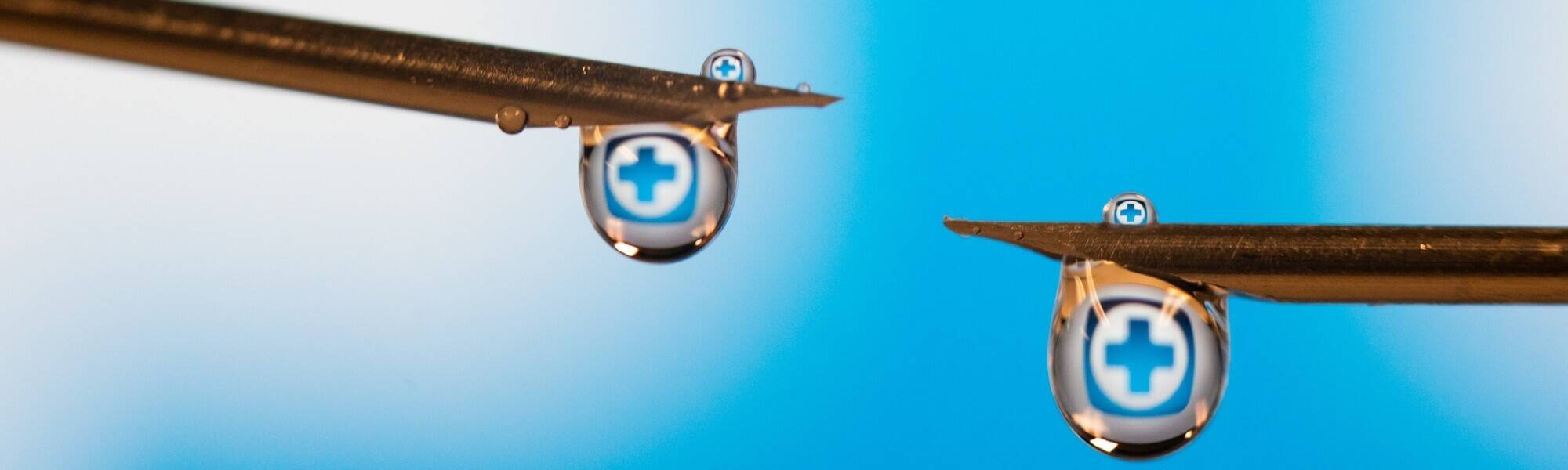 Needles with blue plus sign reflected in droplet of liquid